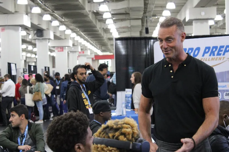 Man speaking to a group of people at a trade show. He is smiling. 